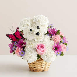 White teddy bear floral arrangement in a wicker basket with pink and purple flowers