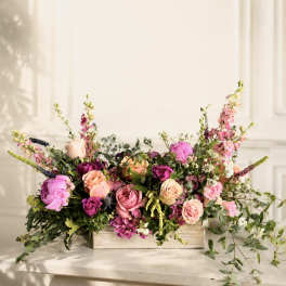 Low floral arrangement of pink and peach roses in a wooden box