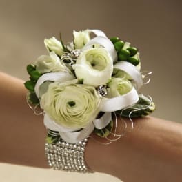 White ranunculus wrist corsage with ribbon and rhinestone bracelet on a person's arm.