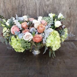 Low floral centerpiece with peach and white roses and pale green hydrangeas in a silver vase