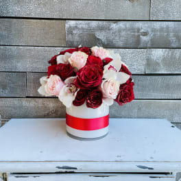 Red and blush roses arranged in a white hatbox with a pink ribbon