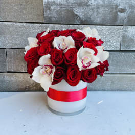 Red roses and white orchids in a white hat box with a red ribbon