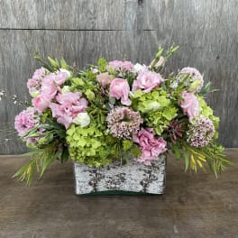 Pink and green floral arrangement in a rustic rectangular container