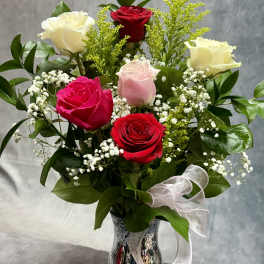 Bouquet of red, pink, and white roses in a silver vase with a white ribbon