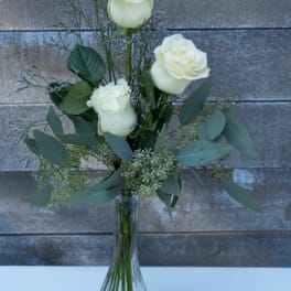 White roses in a clear glass vase with airy purple filler