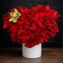 Red rose arrangement in a white vase with a green orchid accent
