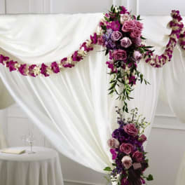 Wedding canopy draped in white fabric with purple and lavender flower clusters and garlands