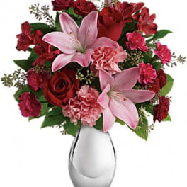 Bouquet of pink lilies, red roses, and carnations in a clear glass vase