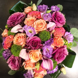 Round bouquet of peach roses, purple blooms, and pink calla lilies
