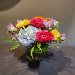 Mixed bouquet with pink roses, blue hydrangea, and yellow daisies in a glass vase