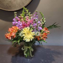 Mixed bouquet in a glass vase with orange, pink, purple, and yellow flowers