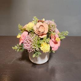 Small floral arrangement in a textured white pot with pink and yellow blooms