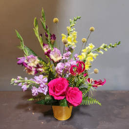 Bright mixed bouquet with pink roses and yellow snapdragons in a gold vase