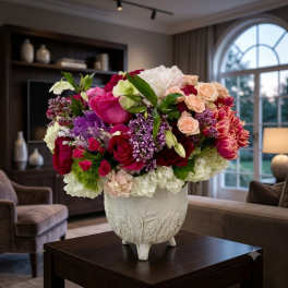 Mixed bouquet of pink, peach, white, and purple flowers in a white vase