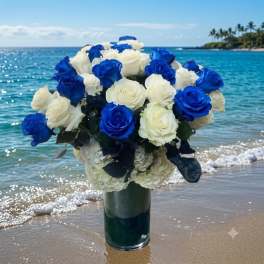 Blue and white rose bouquet in a glass vase on a beach