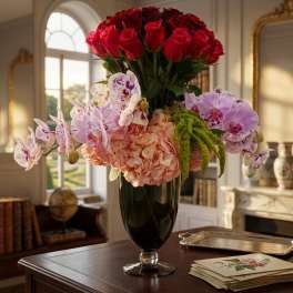 Tall vase arrangement with red roses, pink hydrangeas, and purple orchids