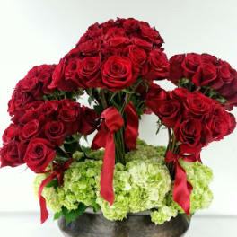Red rose arrangement with green hydrangeas in a dark bowl vase