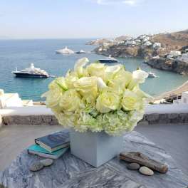 White floral arrangement in a square vase on a table overlooking the sea