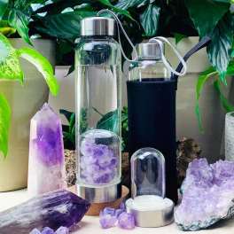 Glass water bottles and purple crystals arranged among potted plants