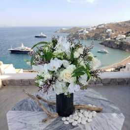 White floral arrangement in a dark vase on a marble table overlooking the sea