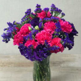 Bright pink carnations and purple flowers arranged in a clear glass vase