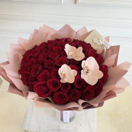 Bouquet of red roses with pale pink orchid accents in pink wrap