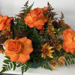 Low arrangement of bright orange roses and golden chrysanthemums in a green container