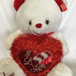 Large white teddy bear with red accents holding a big red heart pillow that says "I love you".