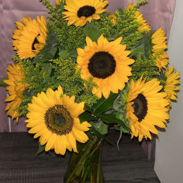 Bouquet of large yellow sunflowers in a clear glass vase on a dark wood surface