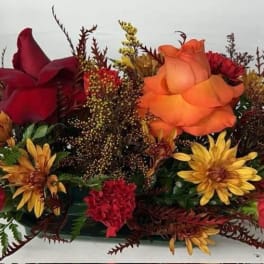 Low centerpiece of red and orange roses, yellow mums, and red carnations in a dark container
