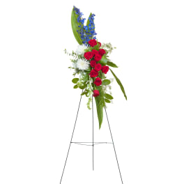Patriotic standing spray with red roses, white mums, and blue delphinium on a metal easel.