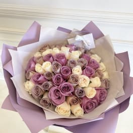 Bouquet of pink, lavender, and cream roses wrapped in purple paper