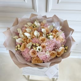 Bouquet of peach roses, pink hydrangeas, and white calla lilies wrapped in blush paper