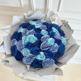 Round bouquet of blue and lavender roses wrapped in pale paper