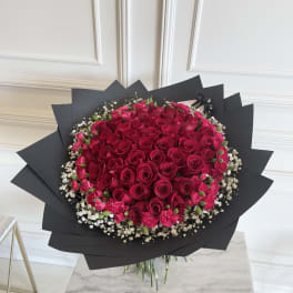 Large bouquet of red roses with pink carnations and white baby's breath in black wrap