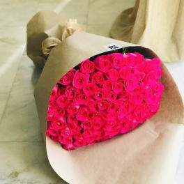 Large bouquet of bright pink roses wrapped in brown kraft paper and ribbon