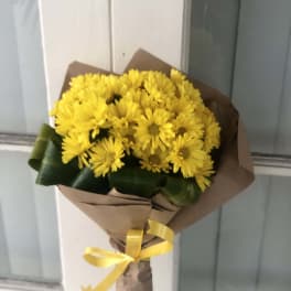 Bouquet of yellow daisies wrapped in brown paper with a yellow ribbon