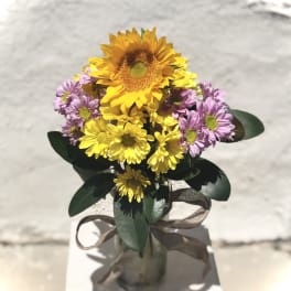 Bouquet of yellow sunflowers and purple daisies in a glass vase