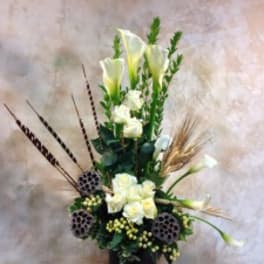Tall white floral arrangement in a black vase with calla lilies and lotus pods