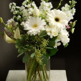 White gerbera daisies and mixed white flowers in a clear glass vase