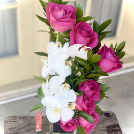 Pink roses and white orchids arranged in a clear glass vase.