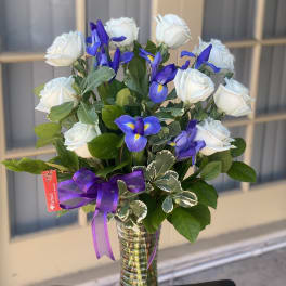 White roses and blue irises in a glass vase with a purple ribbon