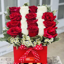 Red and white roses arranged in a red gift box with chocolates and a polka-dot ribbon