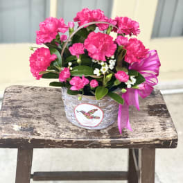 Pink carnations in a woven basket with a ribbon bow