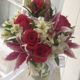 Bouquet of pink roses and lilies in a glass vase with white ribbon