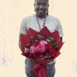 Man holding a bouquet of red and pink roses wrapped in burgundy paper