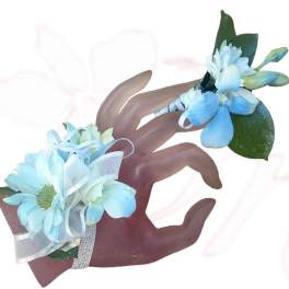 Two blue floral wrist corsages with ribbon on a hand display