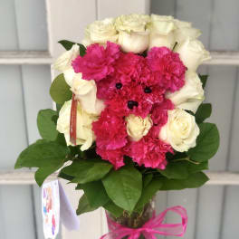 Pink carnations and white roses arranged in a glass vase with a ribbon