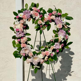 Heart-shaped floral wreath with pink and white flowers on a stand