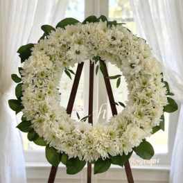 White flower wreath on a wooden easel with green leaves